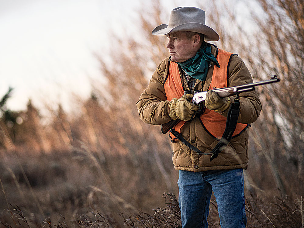 hunter in an orange hunting vest while holding a rifle