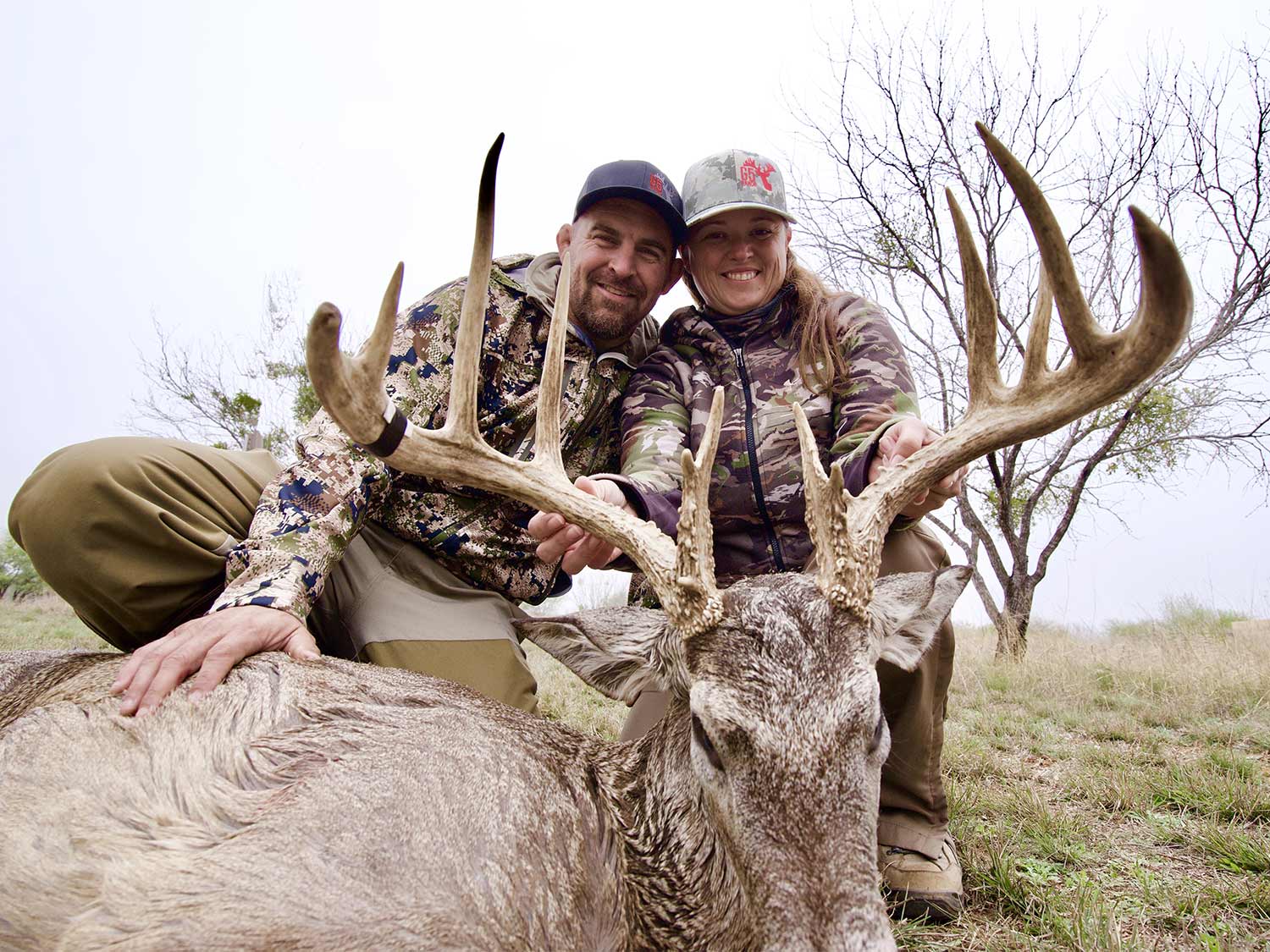 two hunters kneeling behind giant buck antlers