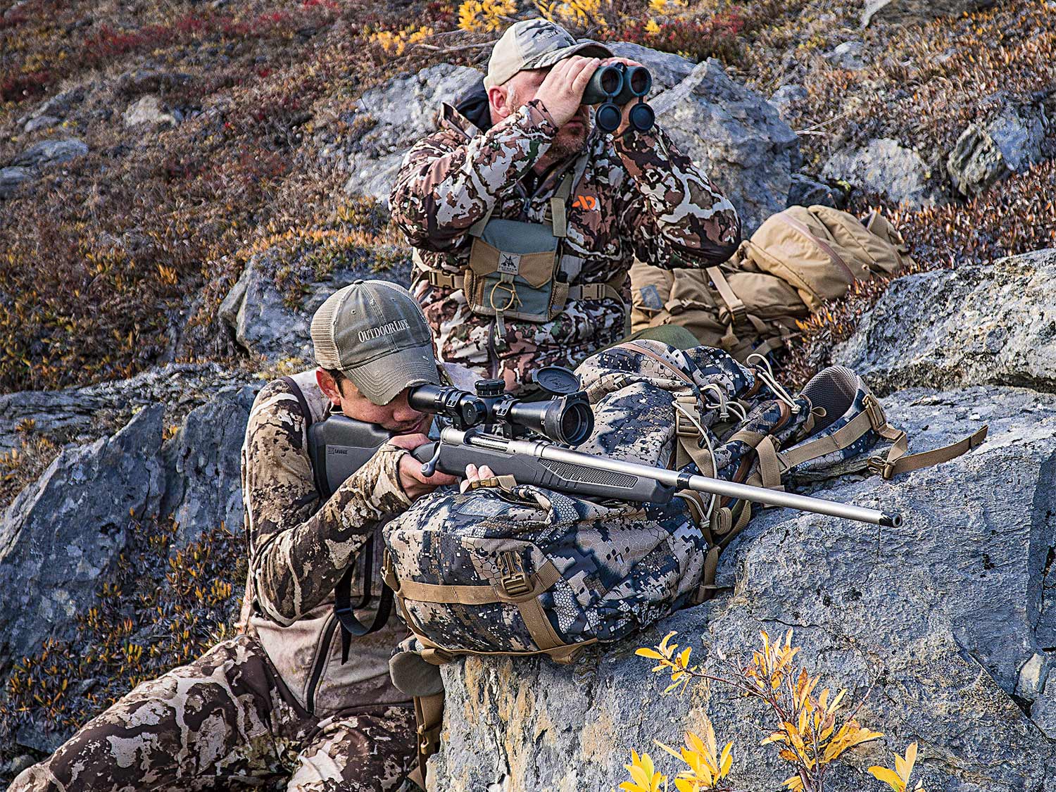 hunter aiming a rifle while another looks through binoculars