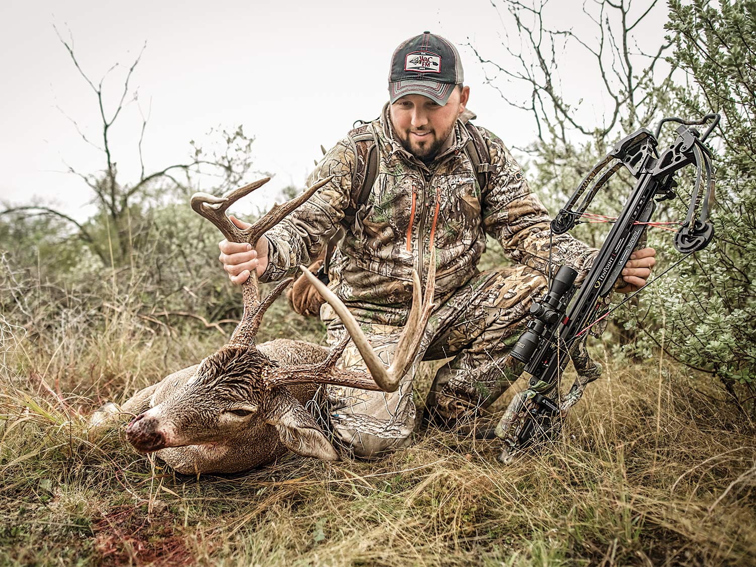 a crossbow hunter kneeling by a buck