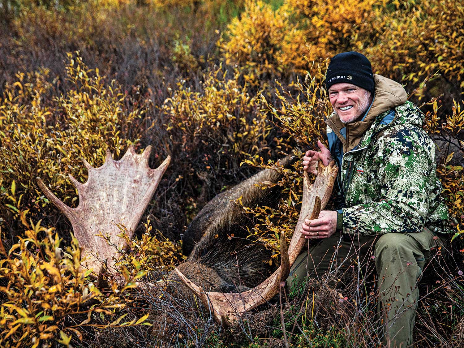 elk hunter kneeling next to large bull elk