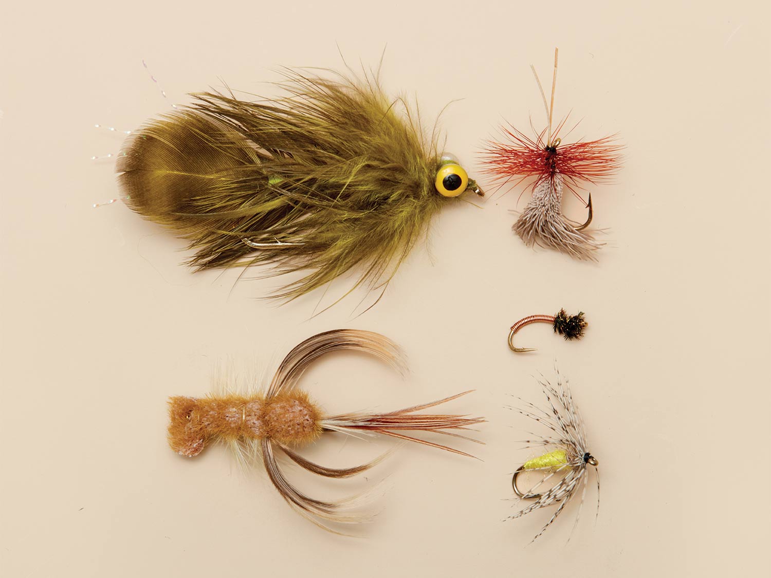 5 old school trout flies on a beige background.