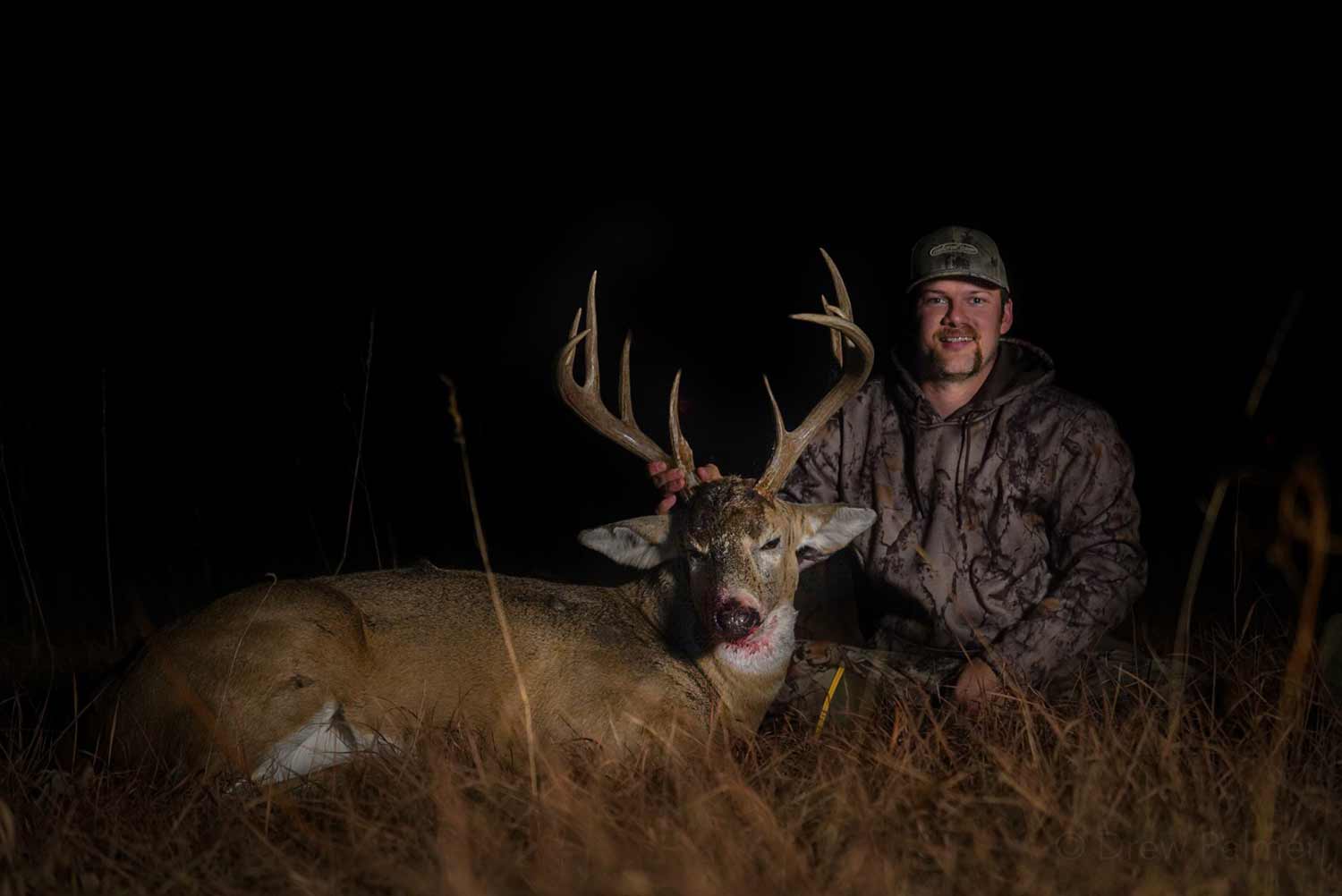 Hunter at knight kneeling next to a deer.