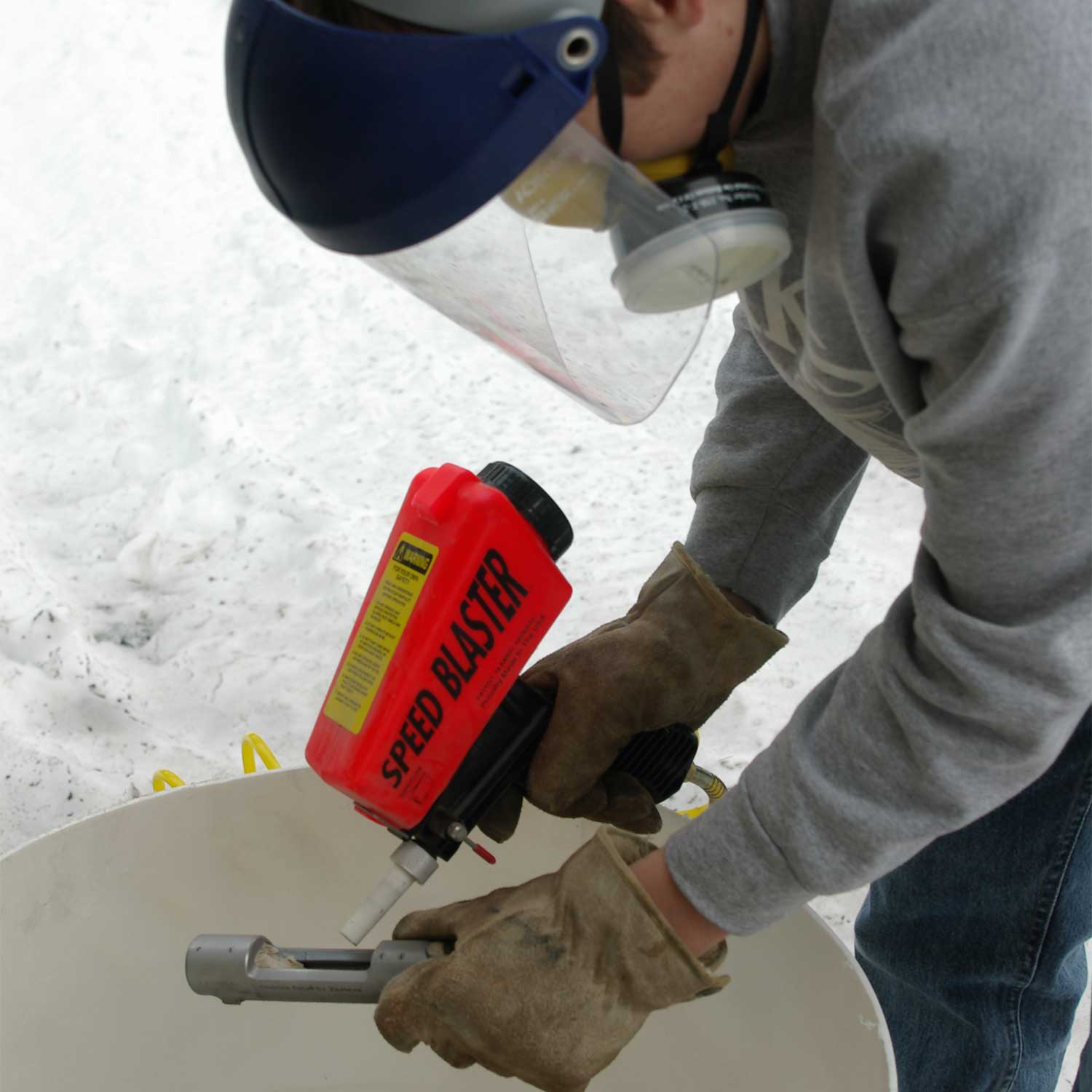 A man using small gravity feed sandblaster to sand a gun.