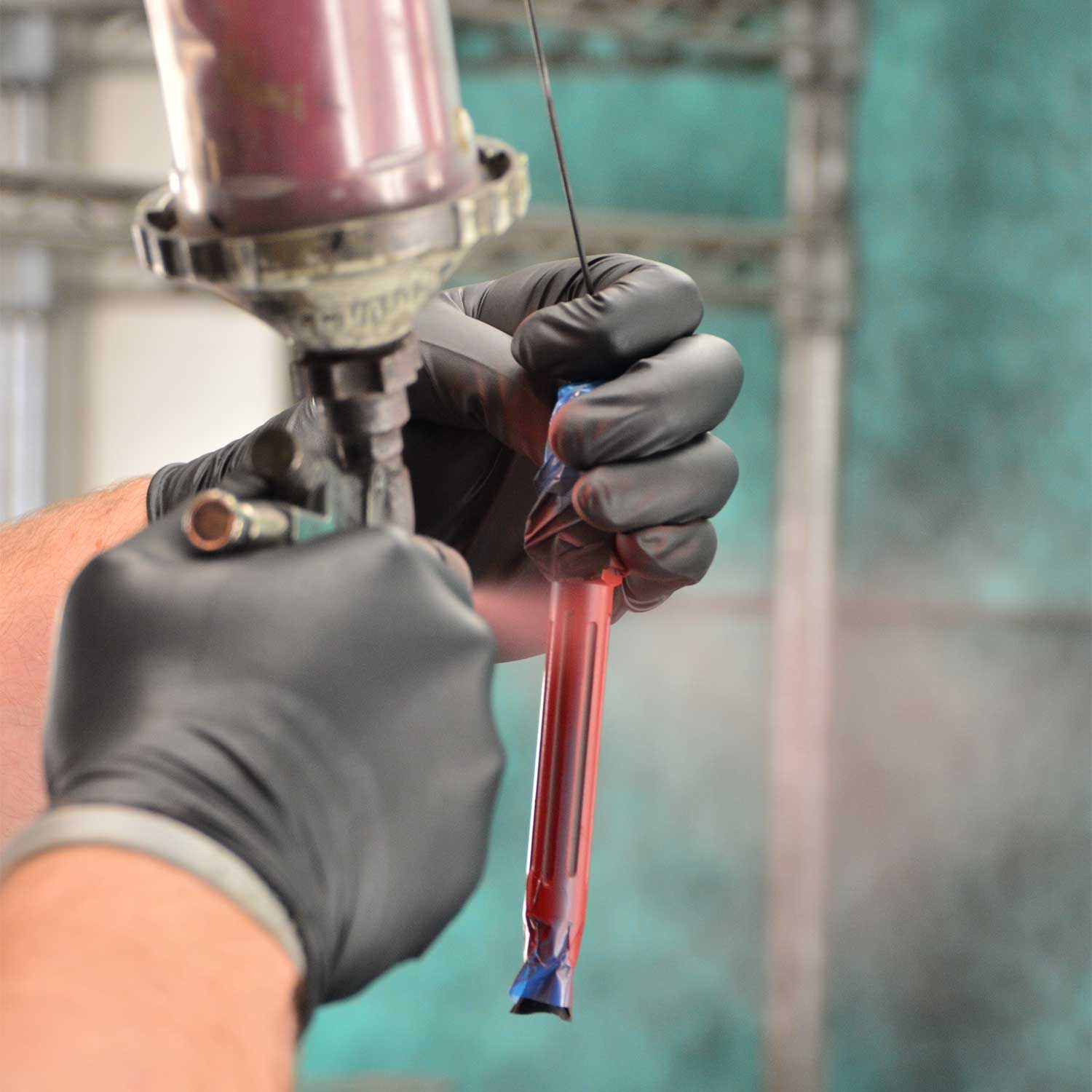 A spray gun spraying red paint on gun parts.