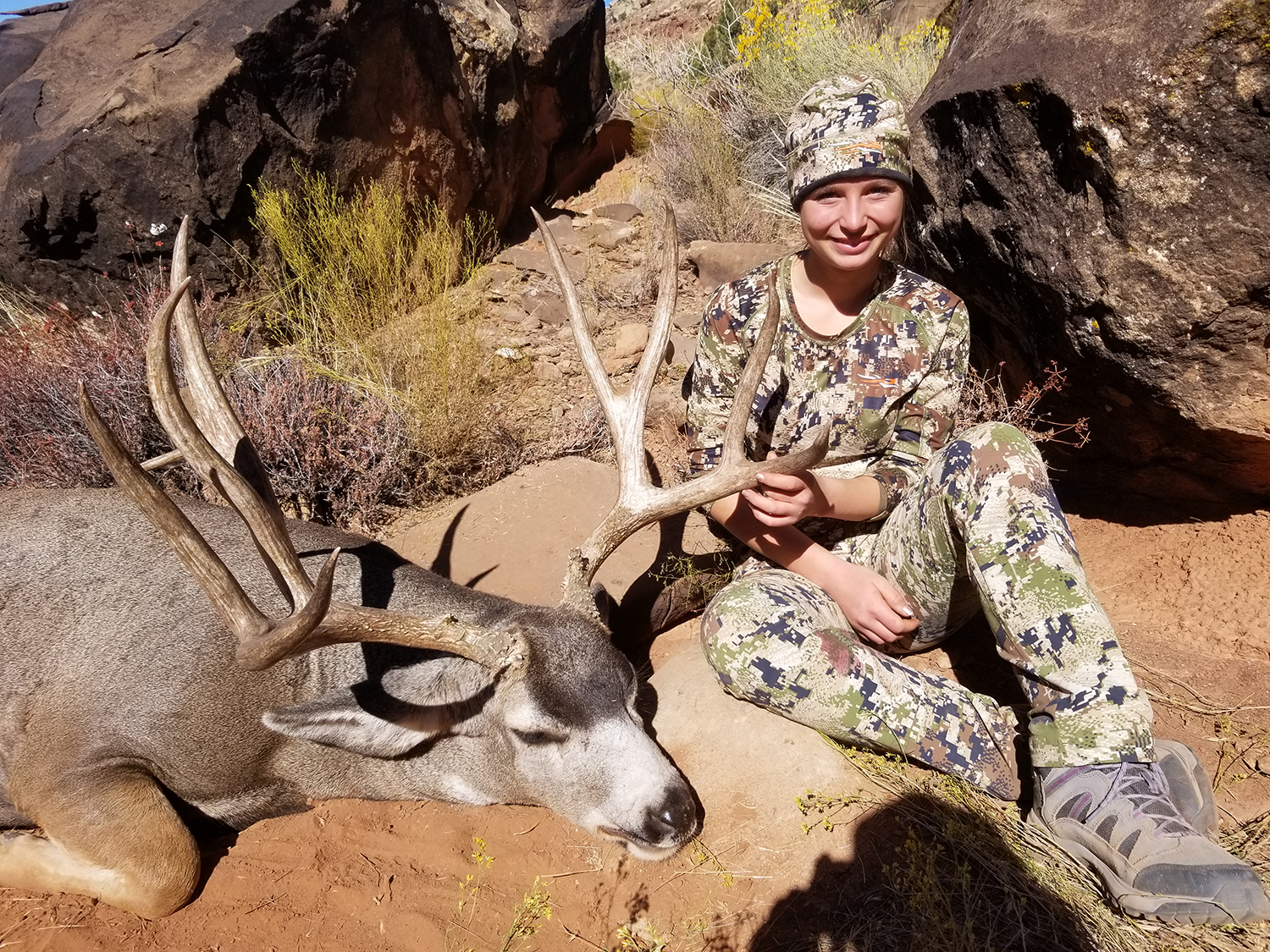 A young girl sits beside a dead buck while holding its antlers