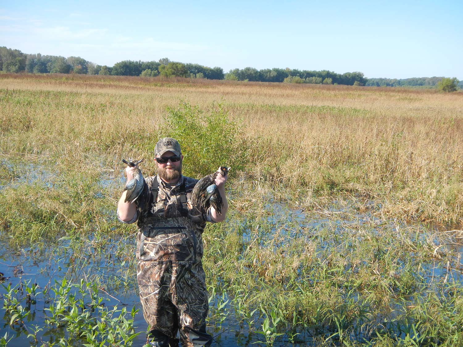 Um caçador segurando patos em um pântano pantanoso