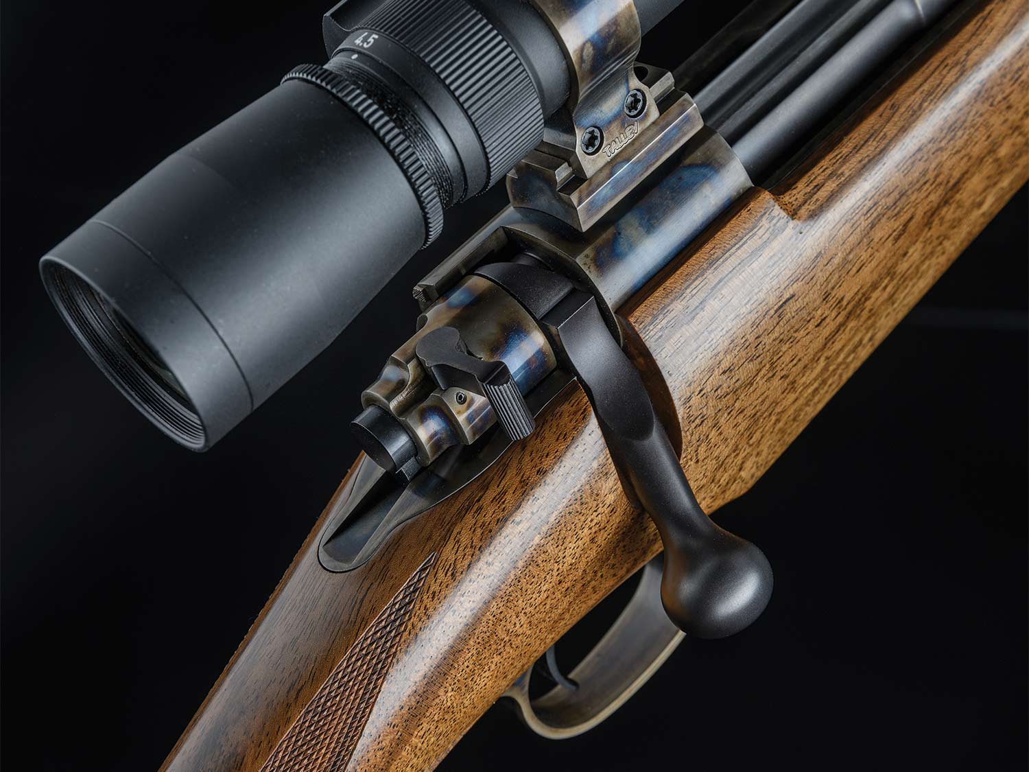 Closeup details of a scoped rifle on a black background.