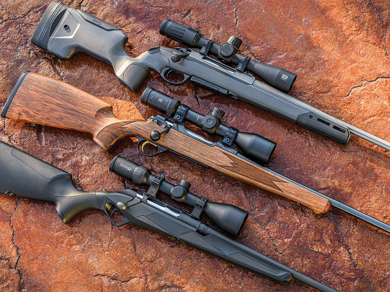 Three rifles arranged and rested on a large flat red stone.