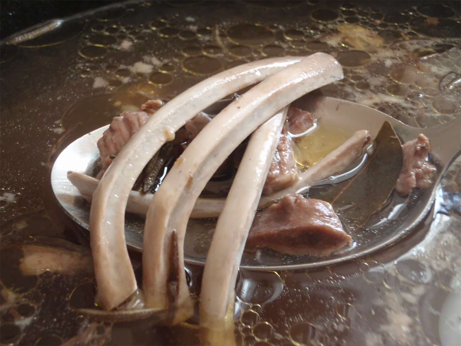 A large pot of bone broth with bits of bones, herbs and meat floating in the broth.