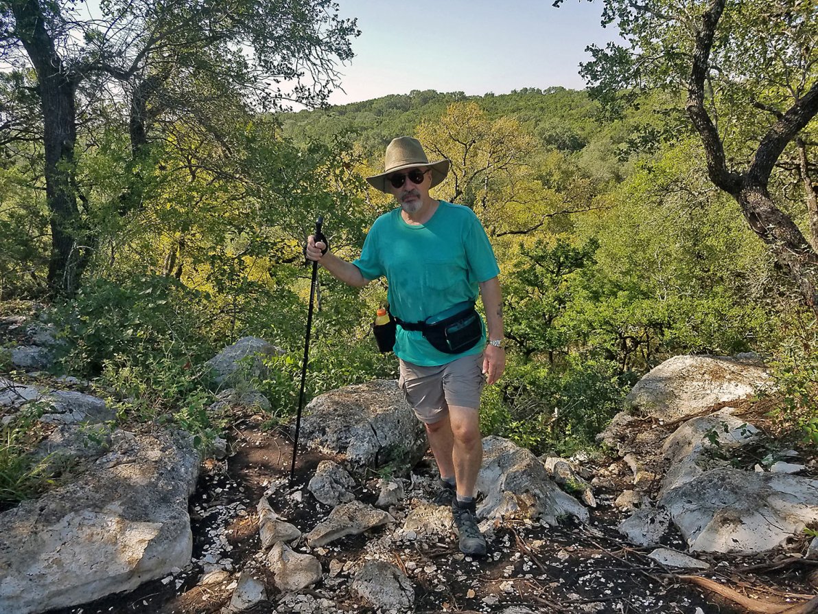 A man hikes through the woods wearing a fanny pack.