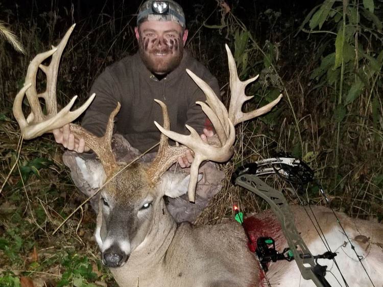 A hunter kneels behind a large whitetail buck at night.