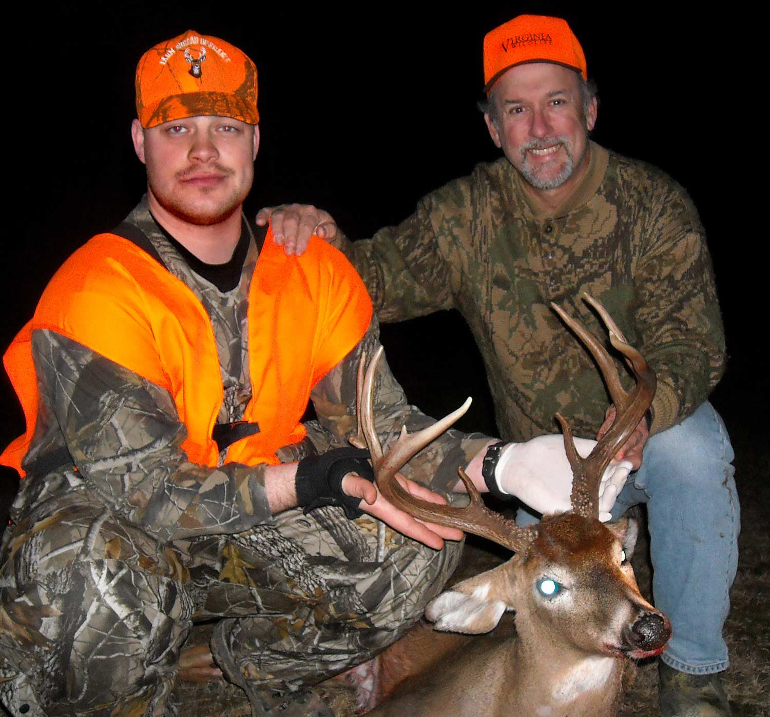 Two hunters kneeling behind a whitetail deer.