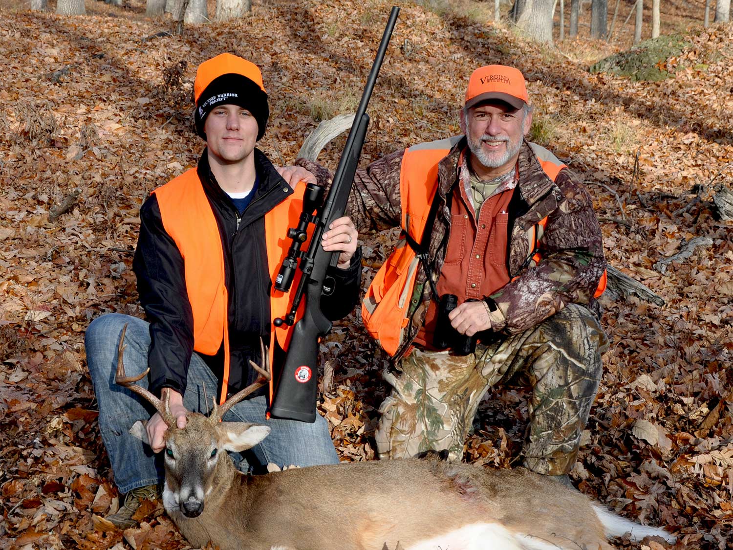 Two kneeling hunters behind a whitetail deer.