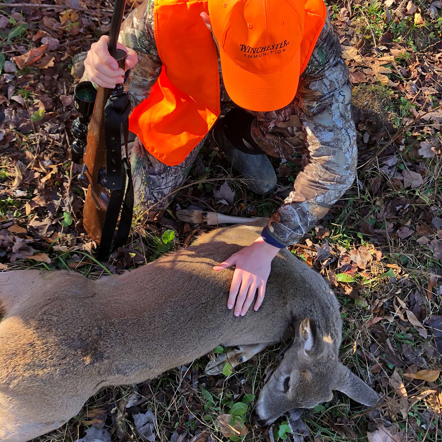 A hunter kneels beside a dropped whitetail deer.