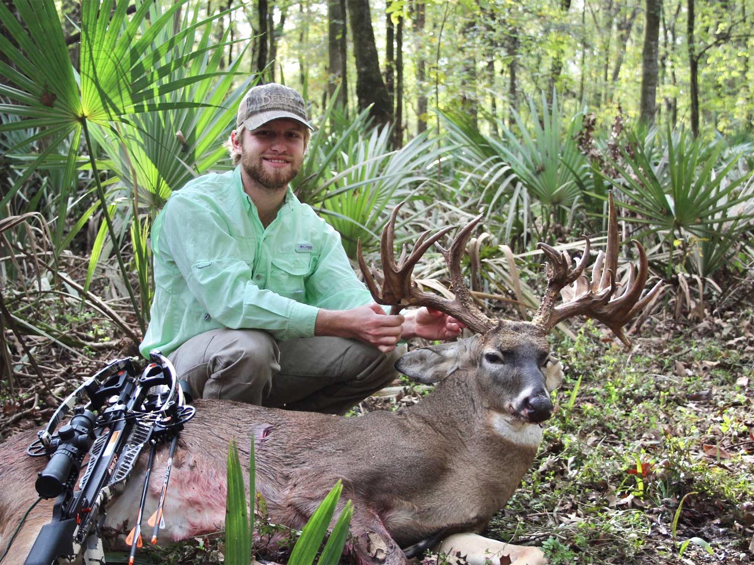 A hunter kneels behind a fallen whitetail deer.