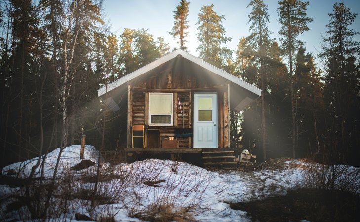 cabin in the woods with sun shining over the roof and snow on the ground