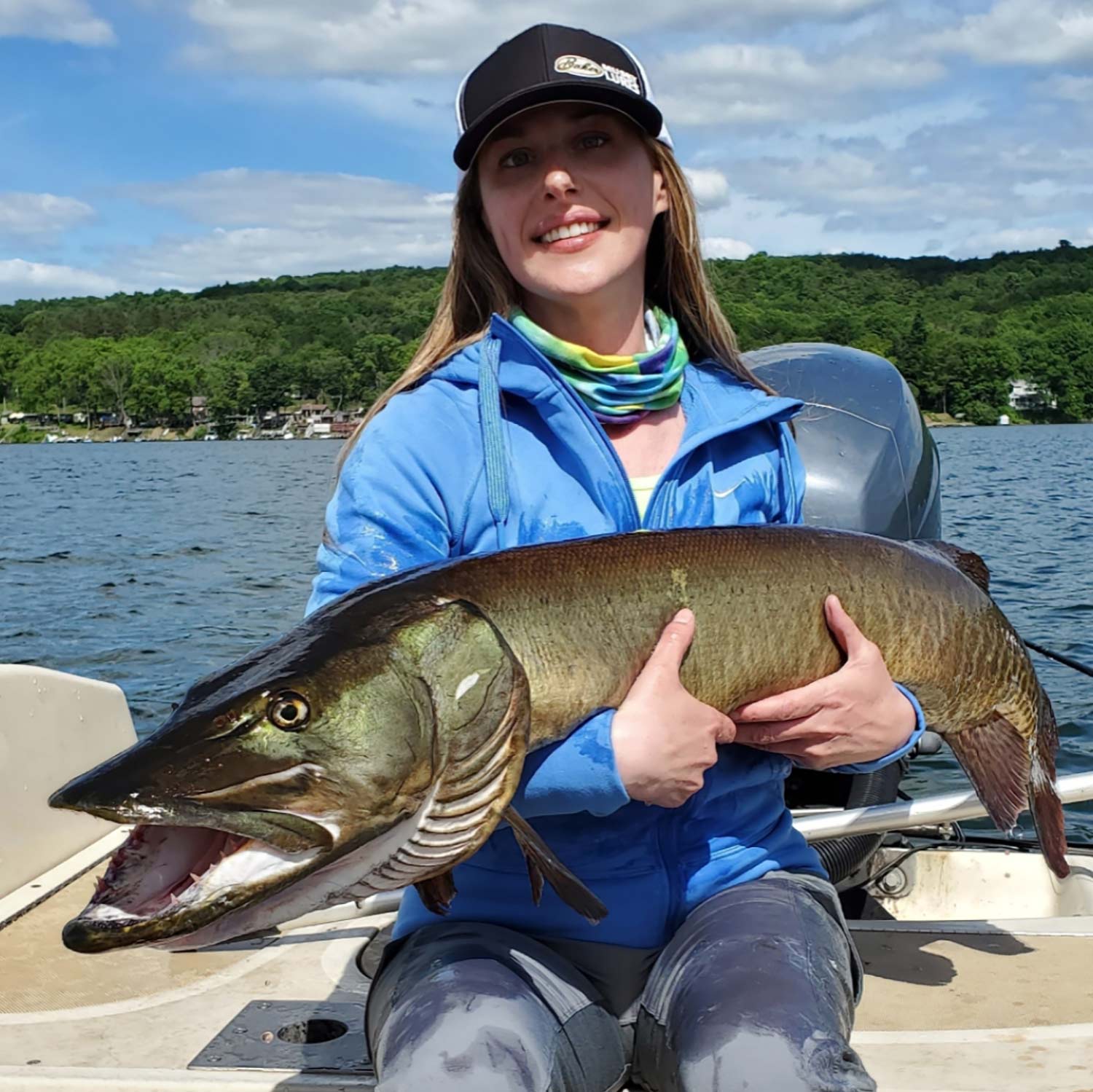 A woman smiles and poses while holding a large muskie fish.