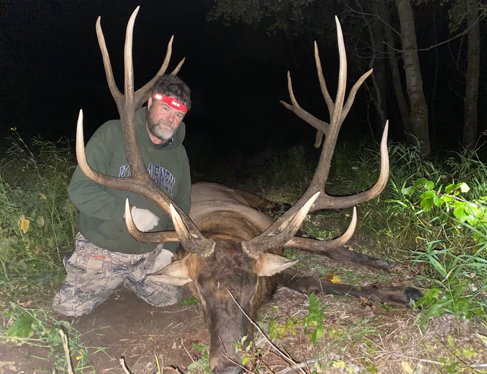 A bowhunt kneels beside a giant record bull elk.