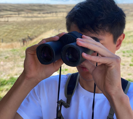 Man in a white shirt holding up a pair of binoculars