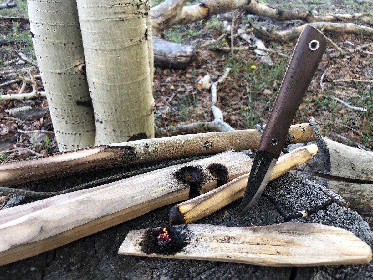 A grey knife with a wood handle stuck in a rock surrounded by pieces of light wood