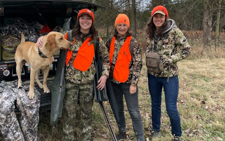 Deer hunters pose with dog on tailgate.