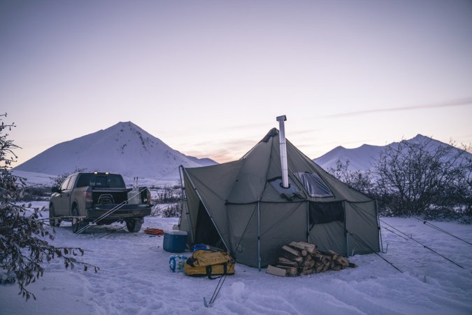 A tall tent with a chimney against a mountain sunset