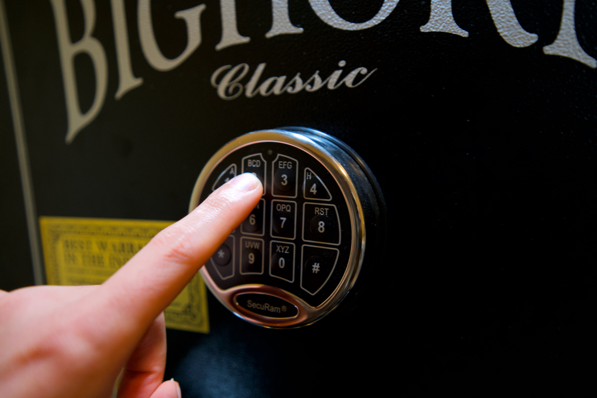 A hand pressing a keypad on a black safe