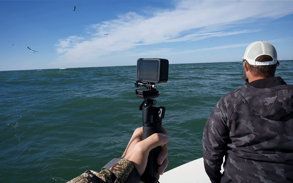 A hand holding a mounted GoPro over the ocean