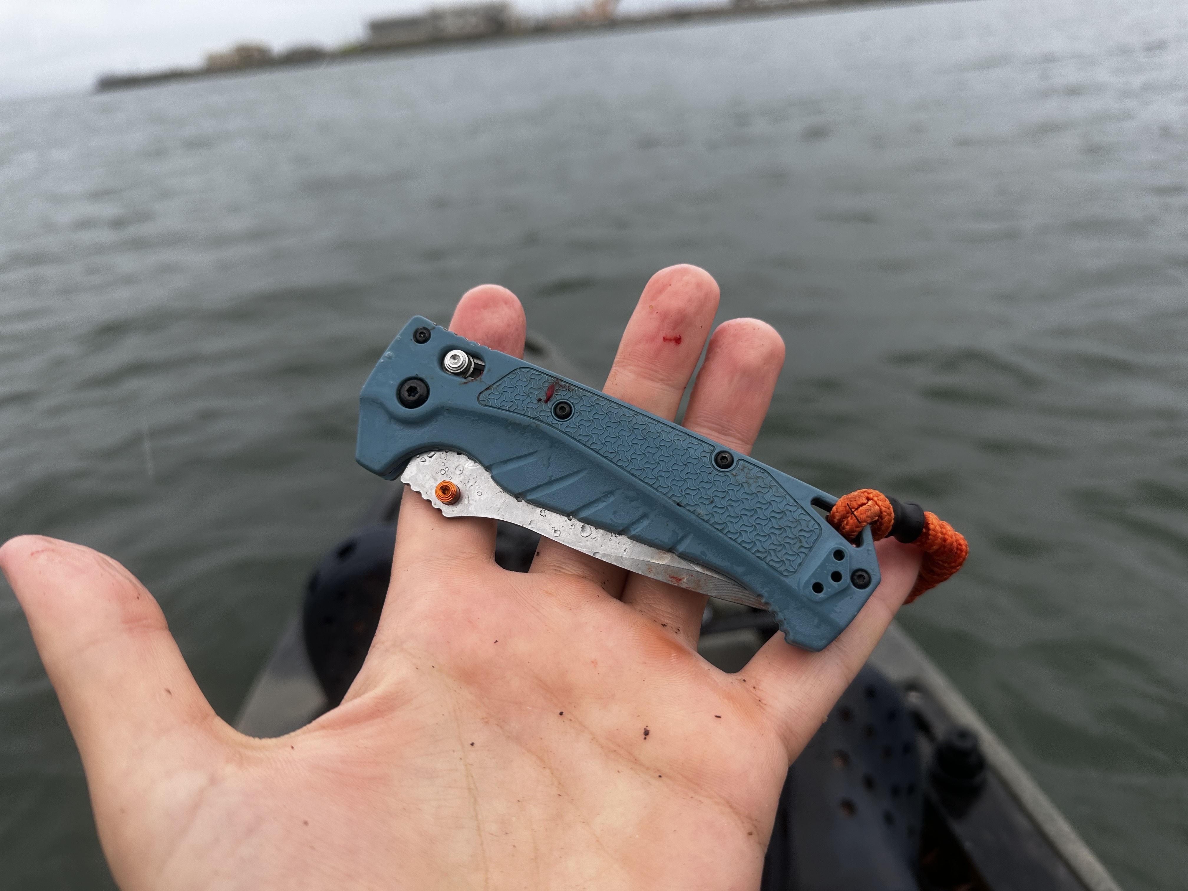 closed knife in open palm with kayak nose and lake in background