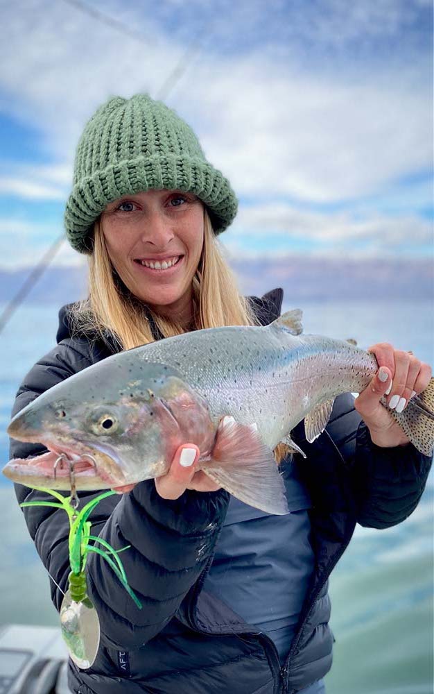 A woman holding a large trout with a green lure in its mouth