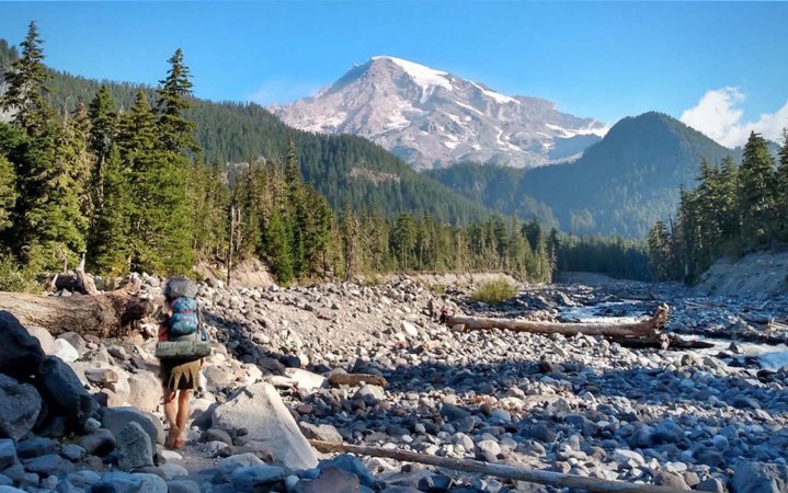 A person with a backpack on walking in the distance toward a large mountain