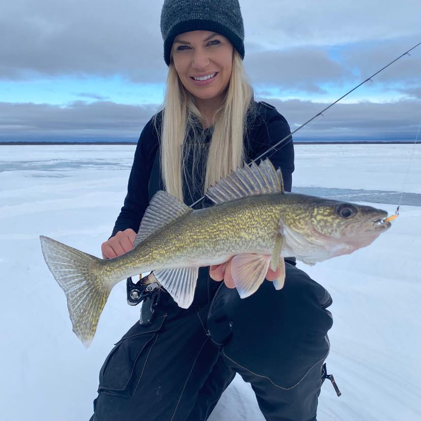 A woman holding a walleye on a frozen lake