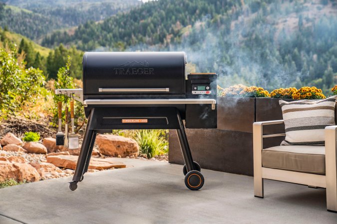 A black best pellet smoker smoking on a patio overlooking trees