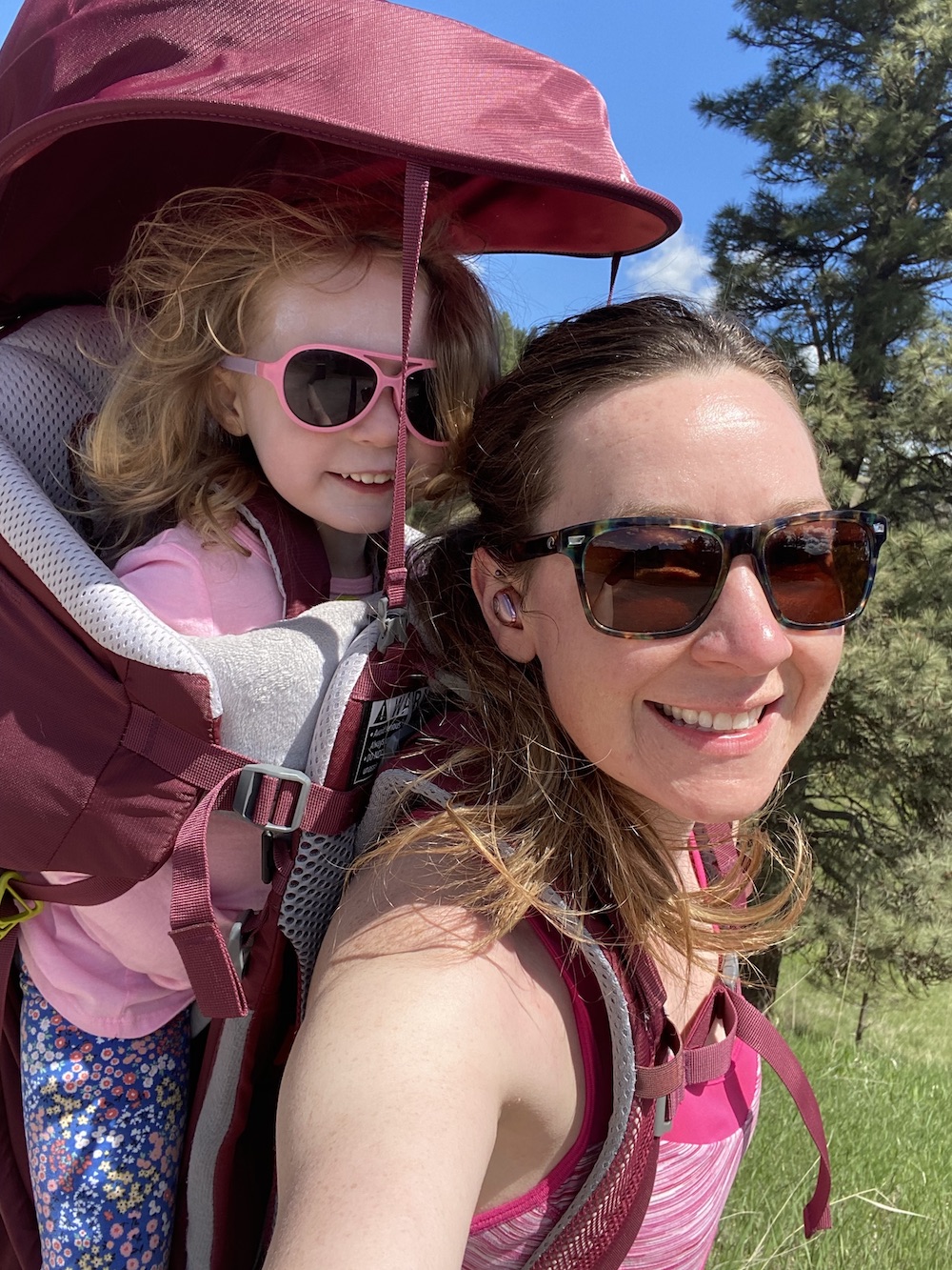 A woman carrying a child in a red backpack smiling