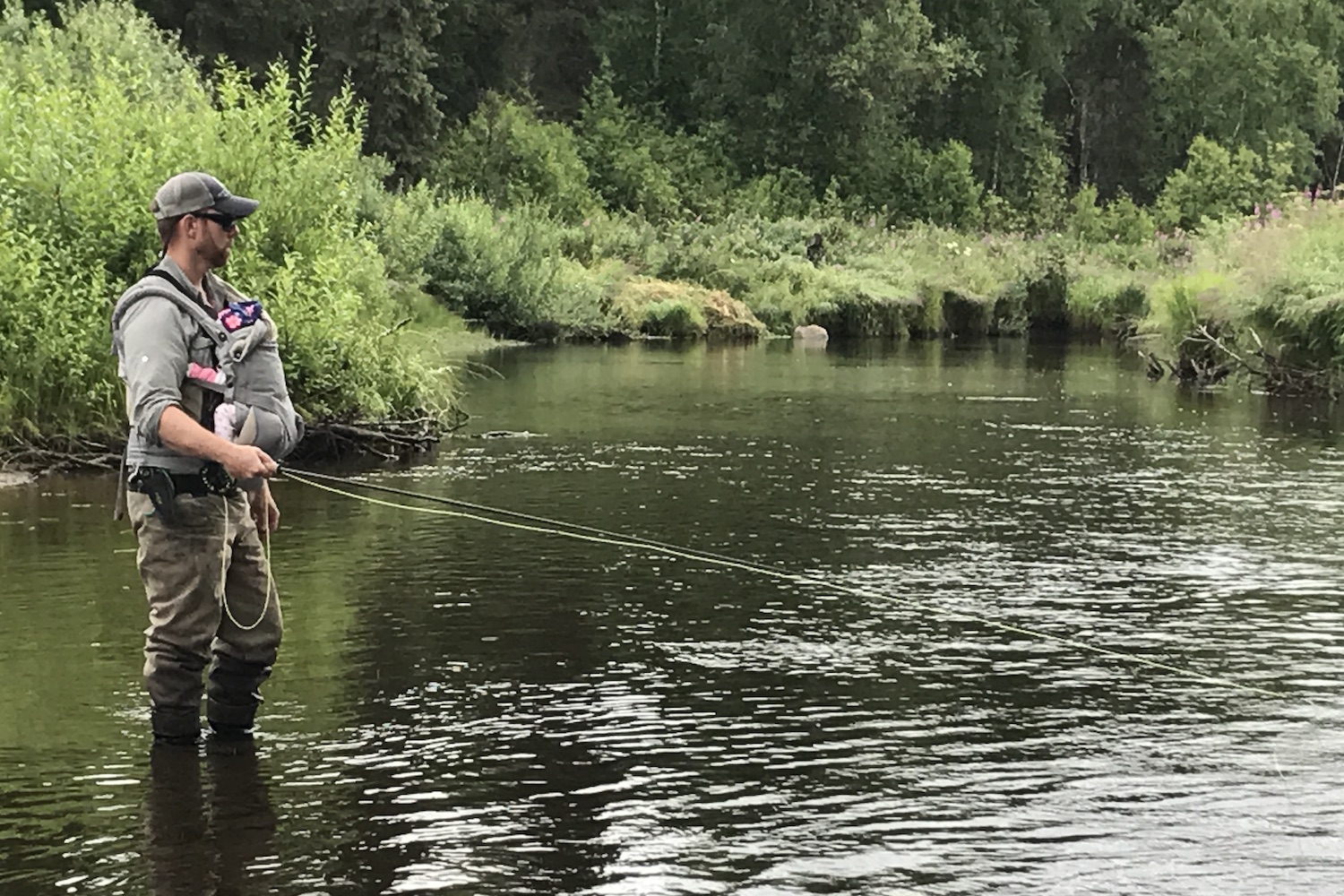 A man with a baby strapped to his chest fishing