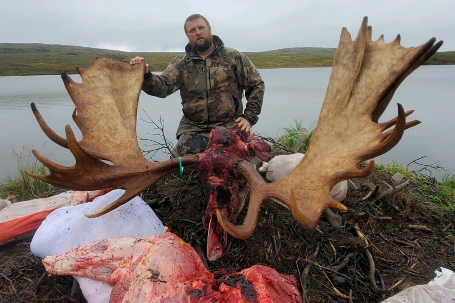 hunter with moose rack and meat at edge of lake