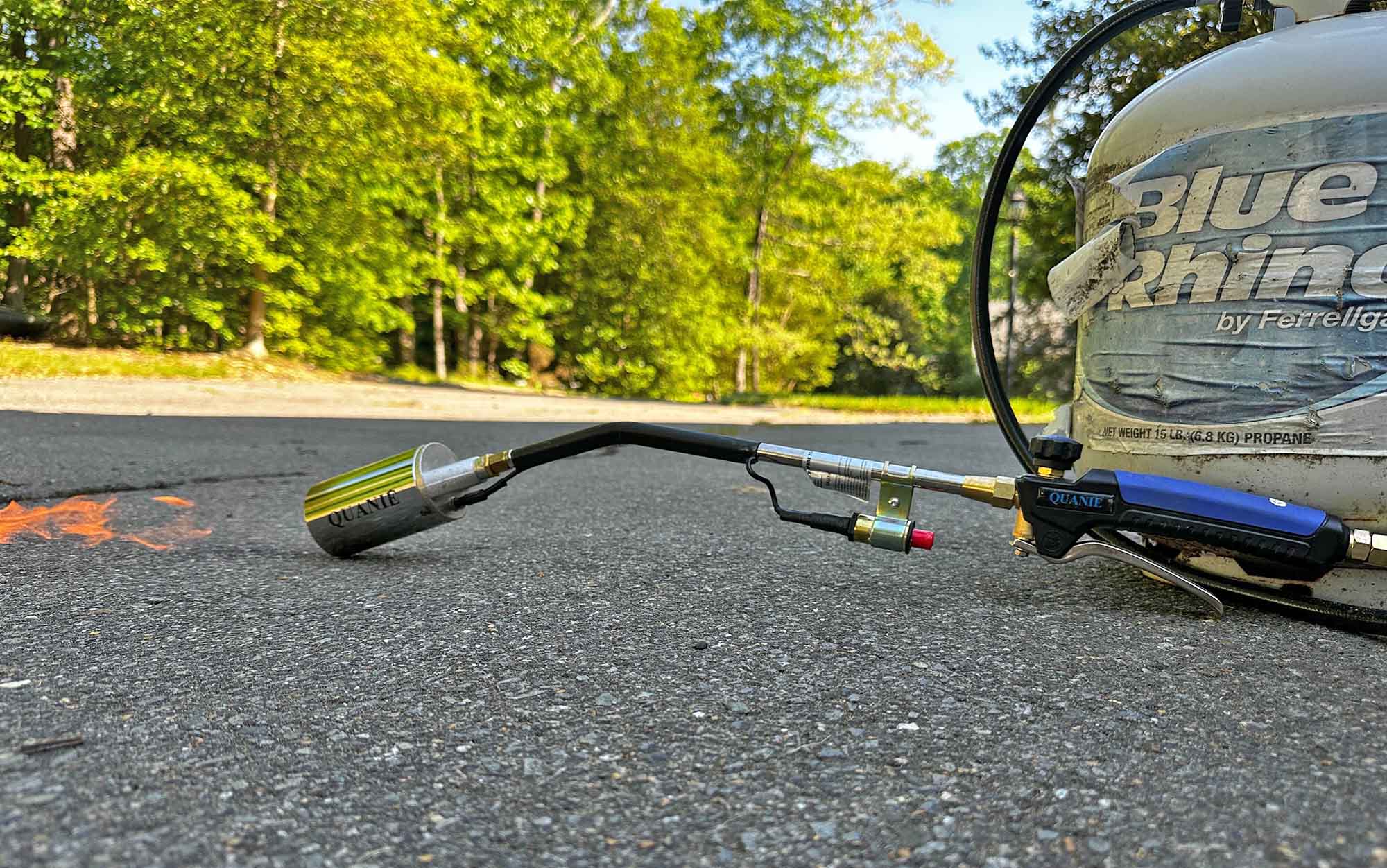 The Quanie 1,200,000 BTU Propane weed Torch sits on blacktop.