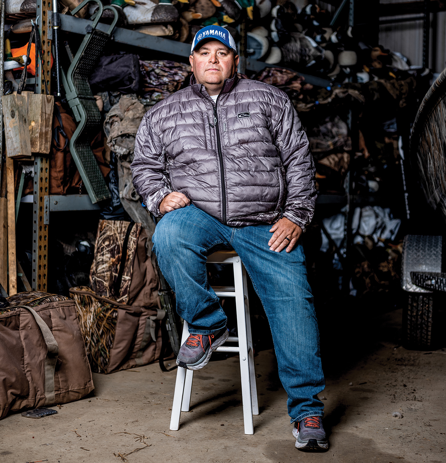 bill lowen sits on a stool in a gargage filled with sporting gear