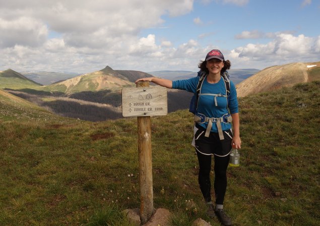 Hiker stands next to trail sign.