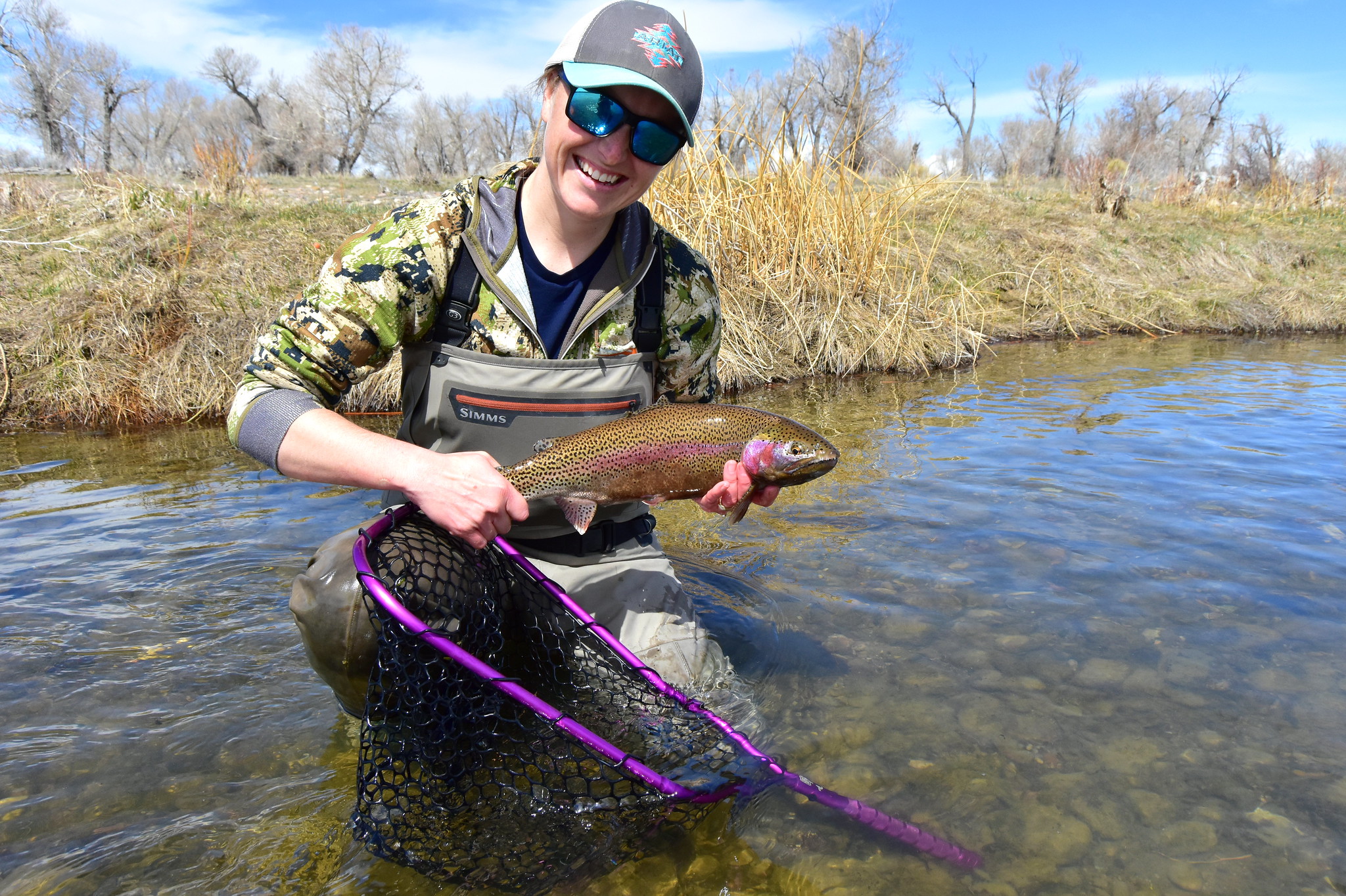 A woman holds up a trout caught on the fly.