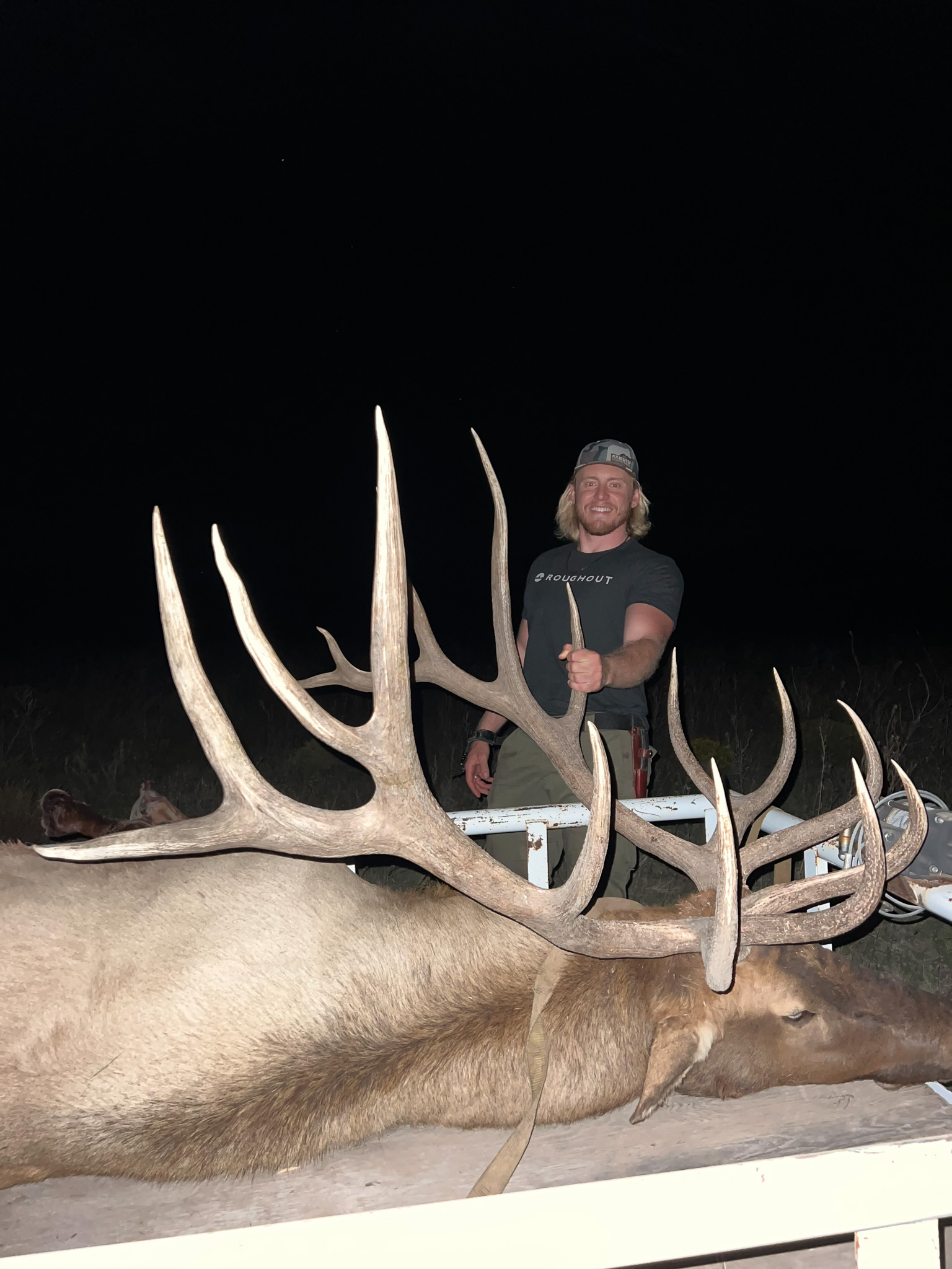 A man stands behind a big bull elk.