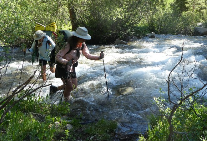 Two women hike across a mountain stream.