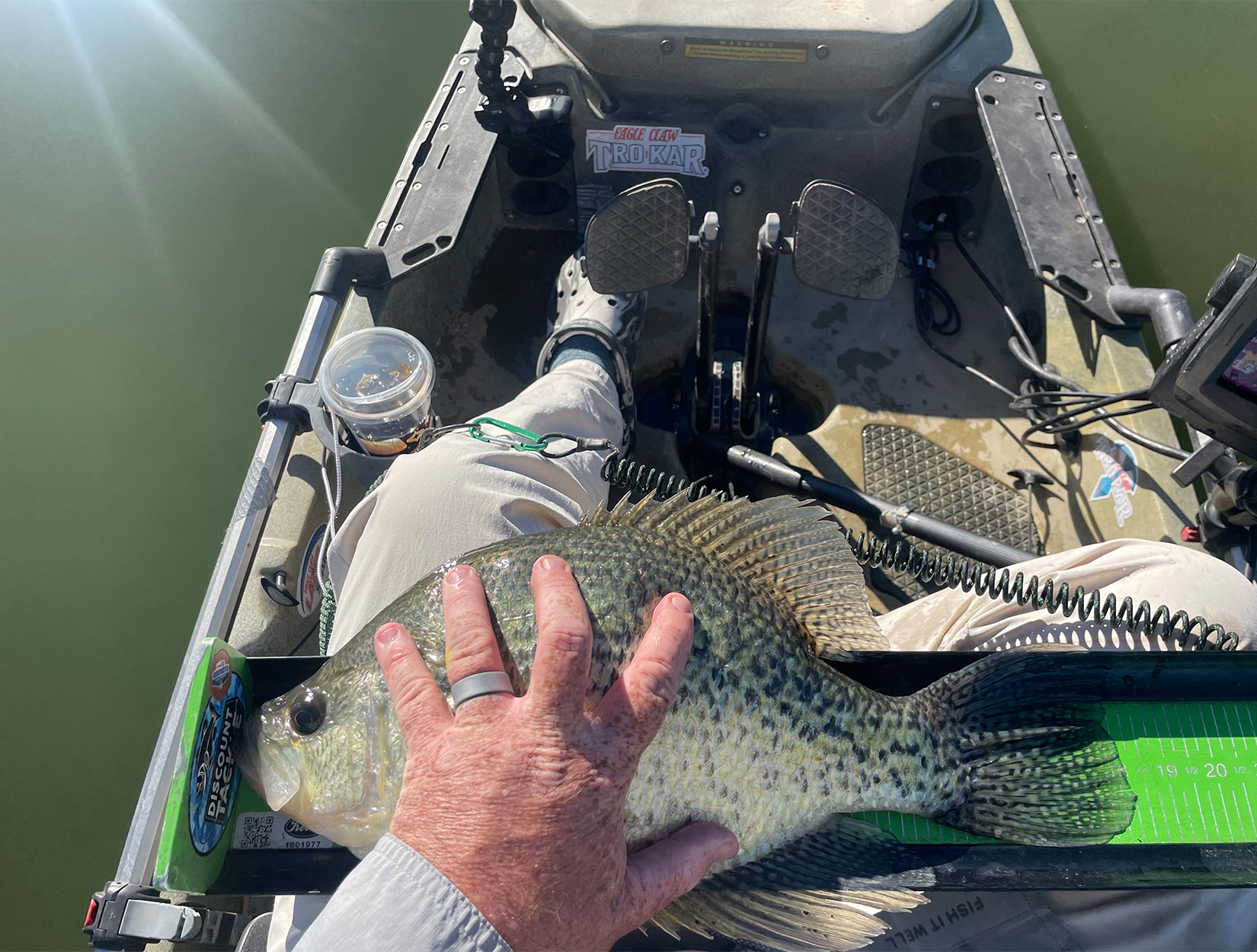 A kayak angler puts his hand on a black crappie for scale.