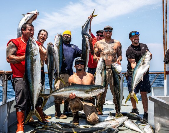 A crew of guys stand on a deck holding and surrounded by yellowtail fish.