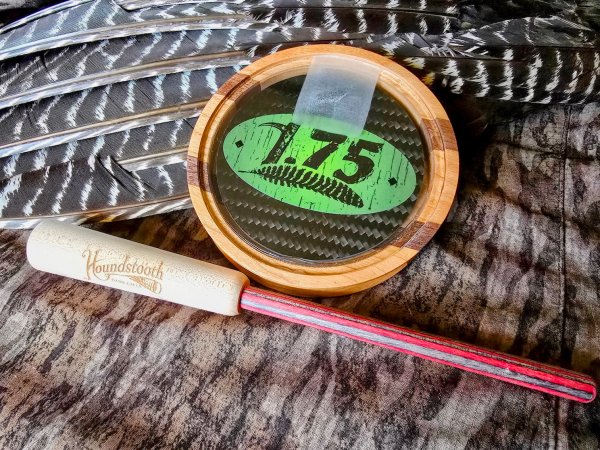  A crystal pot call that says 1.75 leans against a turkey wing next to a wood striker.