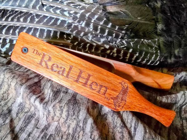  A cherry wood box call that says "The Real Hen" leans against a turkey wing.