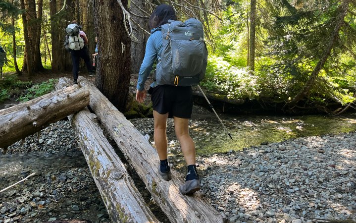  Man hiking across a log wearing barefoot shoes and a backpack