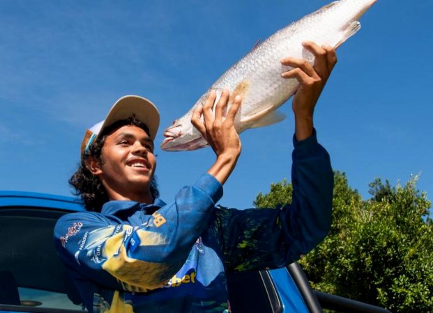 An australian angler holds up a barramundi.