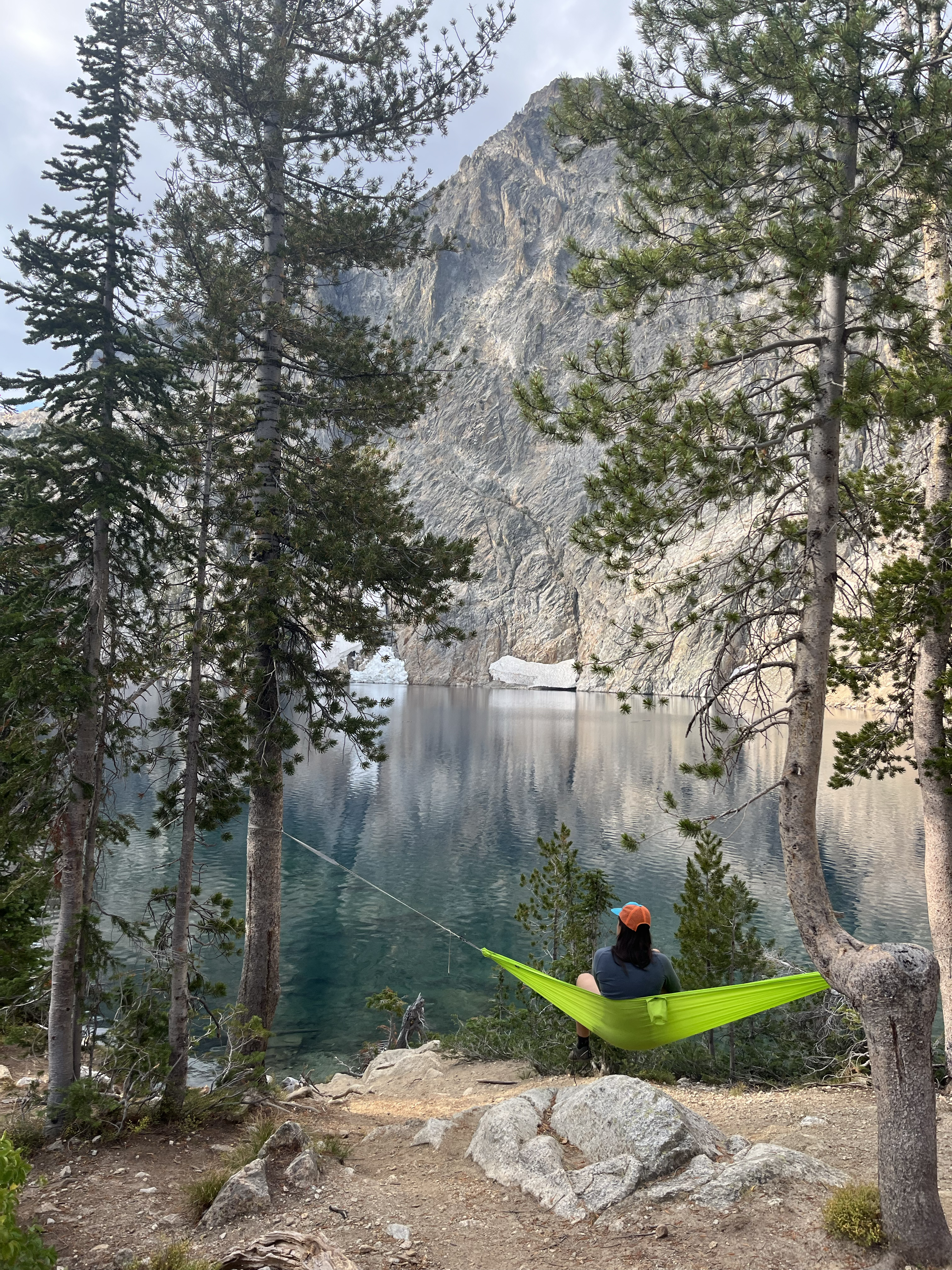 Hiker sits in hammock next to lake.